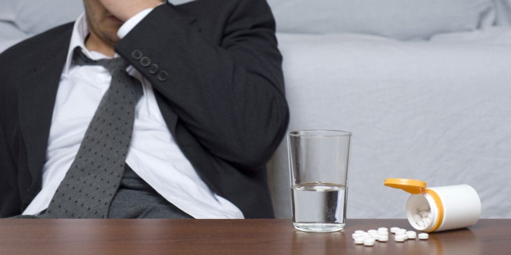 Stressed out businessman with substance abuse triggers sits in front of a bottle of pills