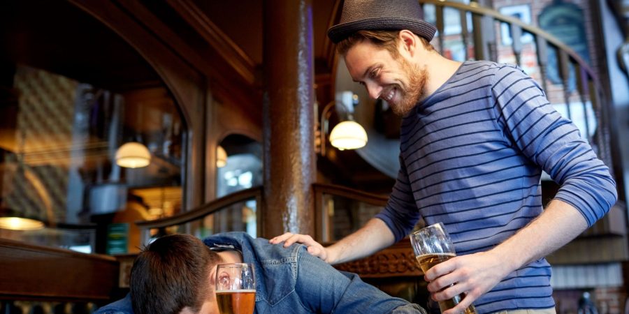 Man drunk and laying on table with friend socially influencing addiction