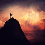 Person who overcame addiction barriers standing triumphantly on top of tall mountain